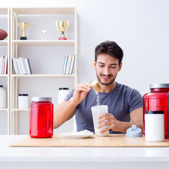 Man mixing a supplement shake in a cup with various supplement containers around him.