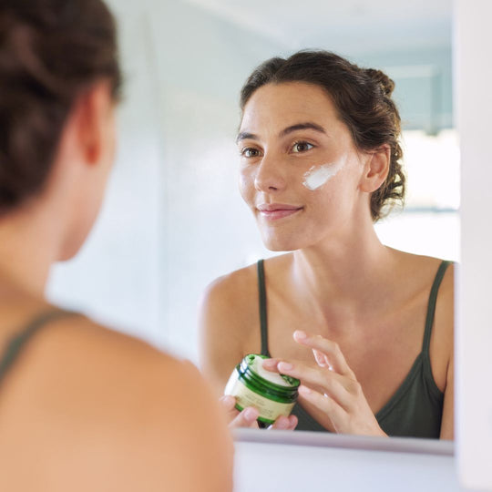 Woman applying cream to her face in front of a mirror